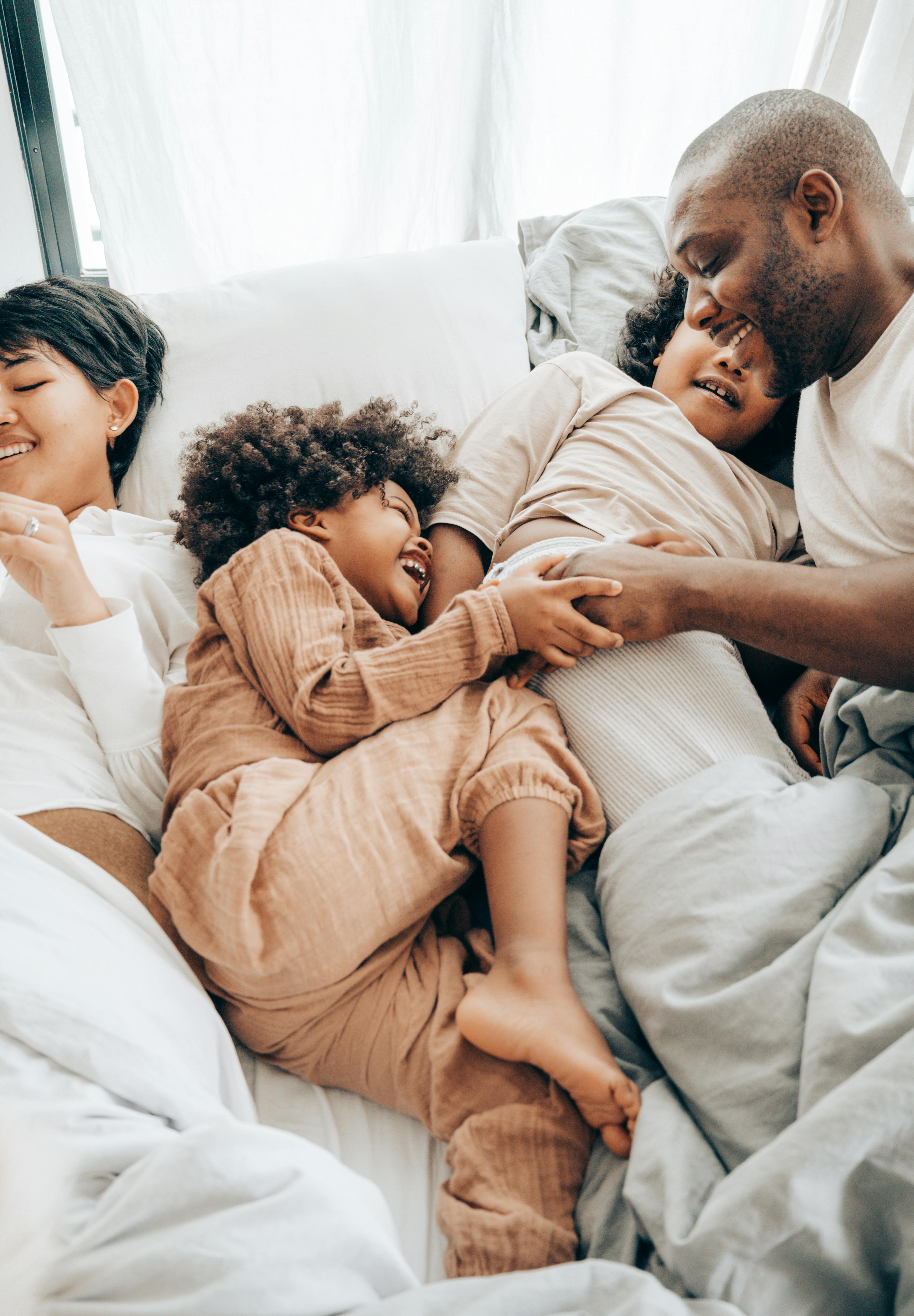 happy african american father playing with children on bed