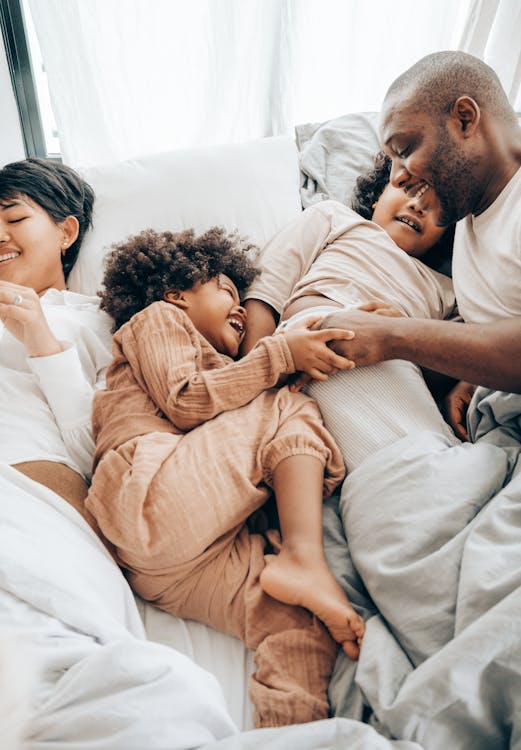 Free From above of smiling ethnic kids playing with father while resting together on bed lying near mother Stock Photo