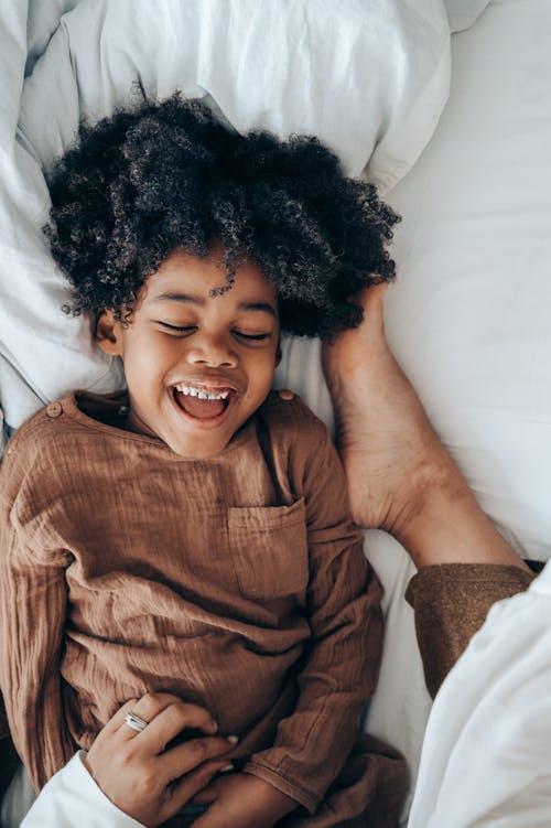 Happy African American boy lying on bed near legs of mom