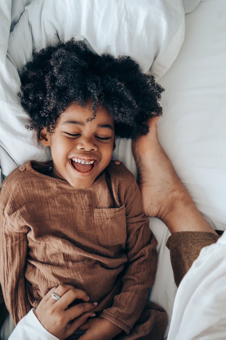 Happy African American Boy Lying On Bed Near Legs Of Mom