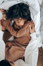 From above side view of cheerful ethnic male kid in nightwear lying on bed and playing with mother