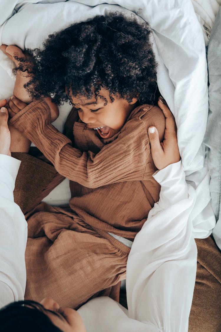 Laughing African American Boy Playing With Mom On Bed