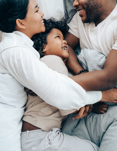 Free Happy ethnic mother and kid hugging father in bed Stock Photo