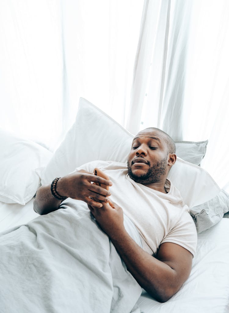 Adult Black Man Using Smartphone In Bed