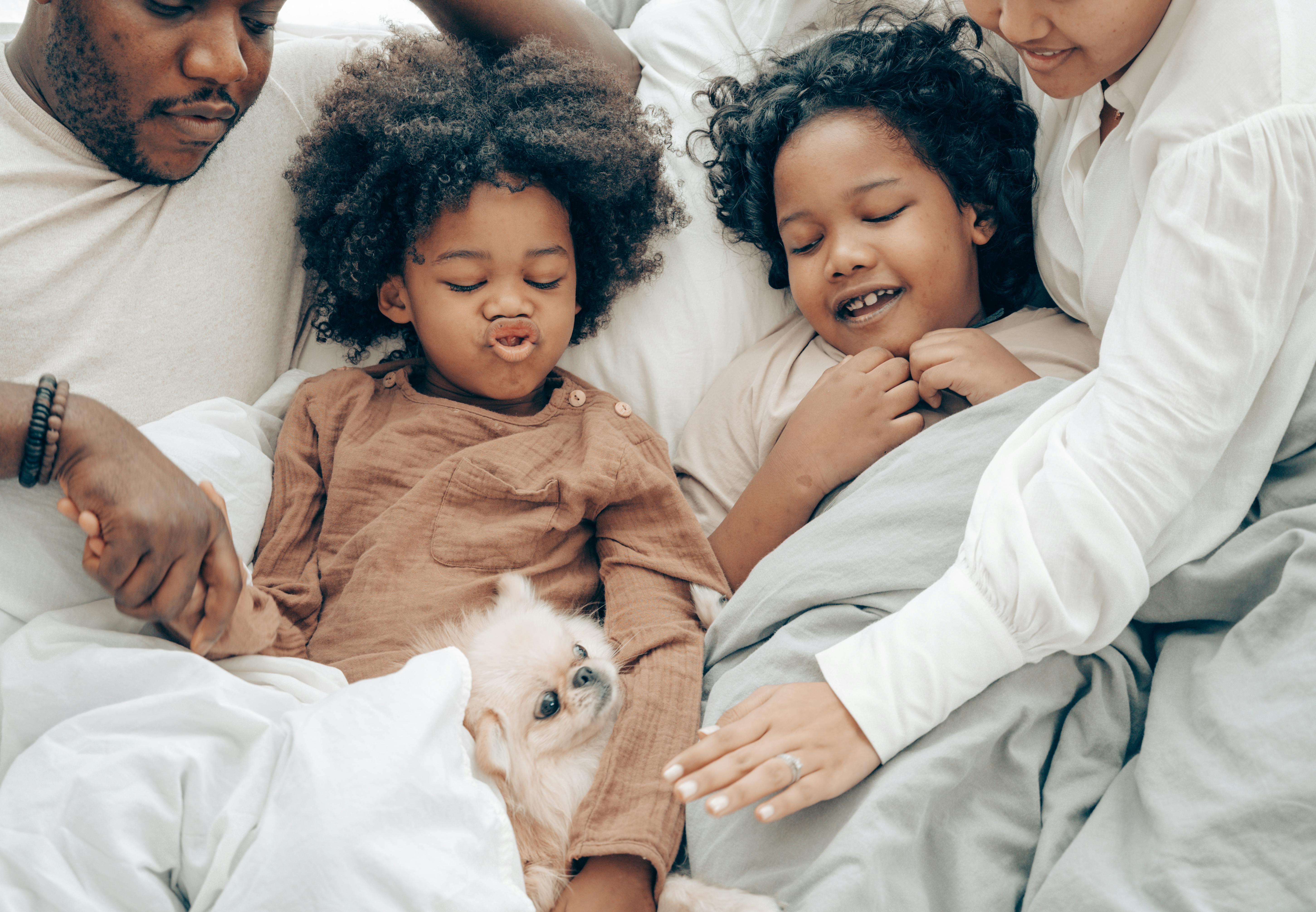 happy ethnic family resting in bed with little dog