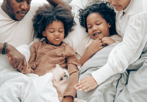 Happy ethnic family resting in bed with little dog