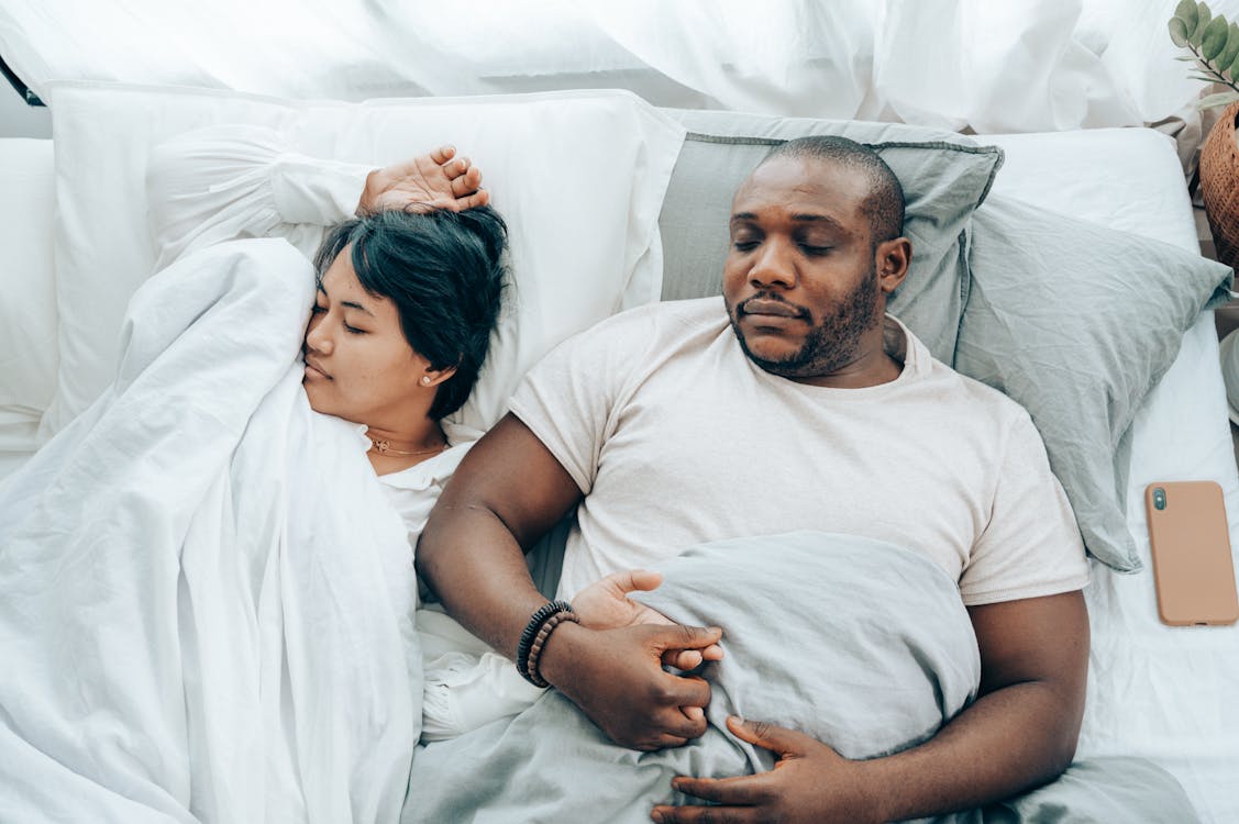 Free Young multiethnic spouses sleeping in bed holding hands Stock Photo