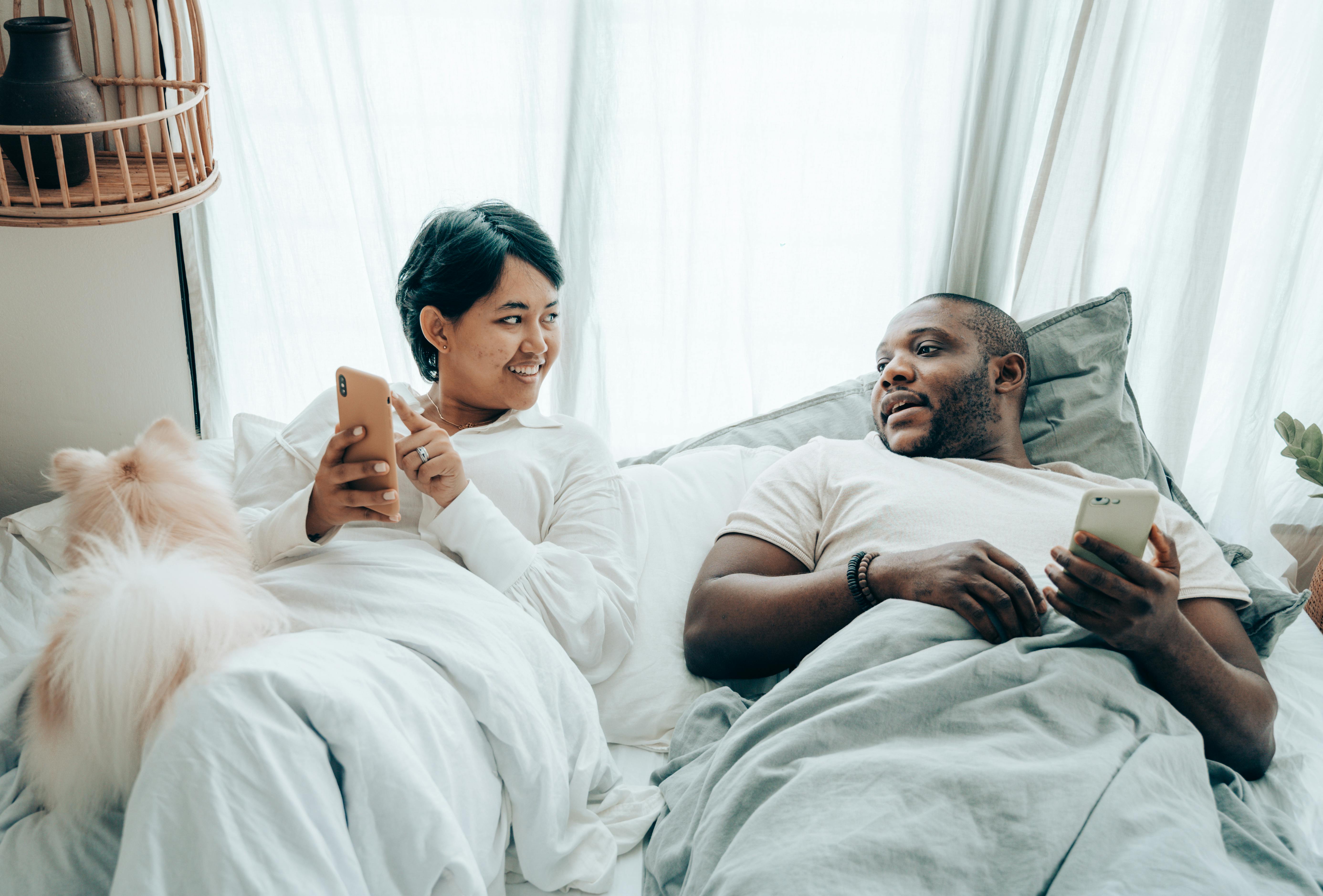 positive young multiethnic spouses communicating while lying in bed