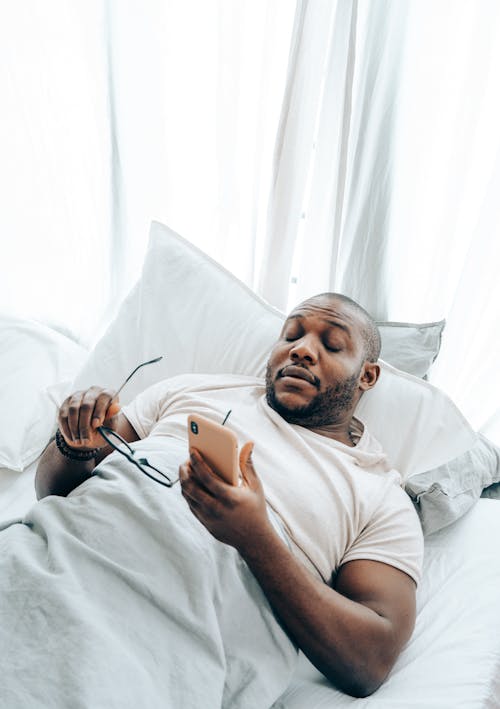 From above of young African American male getting phone call while lying and sleeping in bed