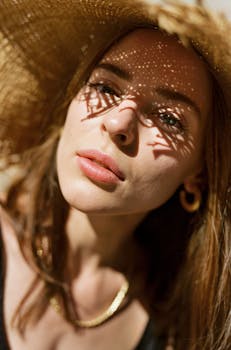 Close-up portrait of a woman wearing a straw hat with intricate shadow play on her face, evoking a summer mood.