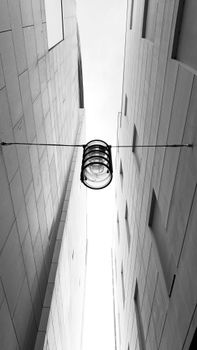 Low angle black and white of high modern multistage building exteriors near wire with hanging lantern in city