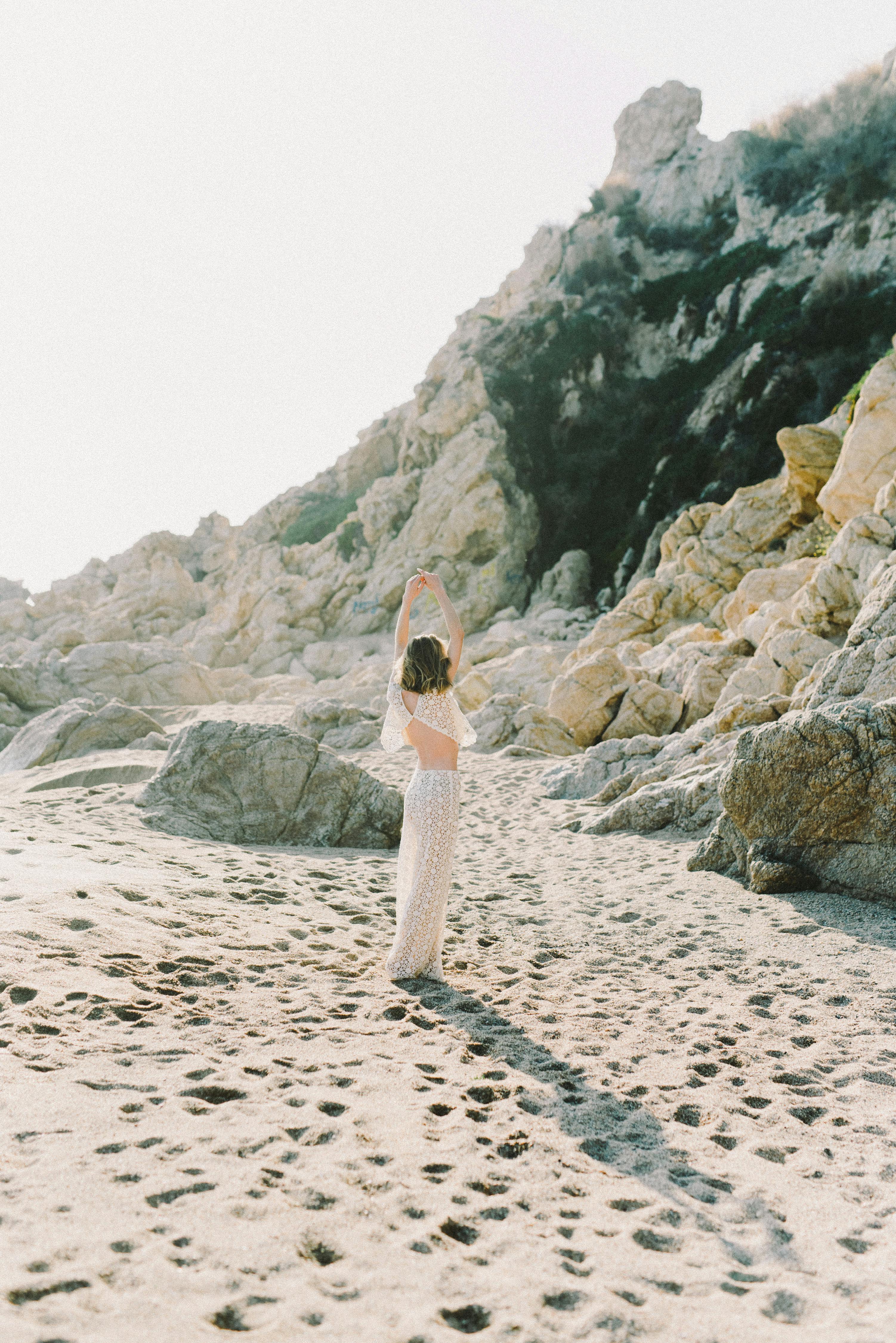 夏日沙滩上，一位金发碧眼的女子优雅地摆着姿势，与自然美景和宁静相映成趣