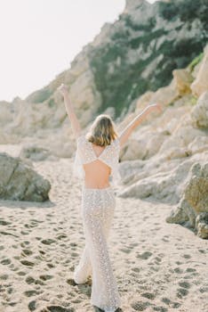 一个女人在夏天的岩石沙滩上举起双臂，享受阳光明媚的散步