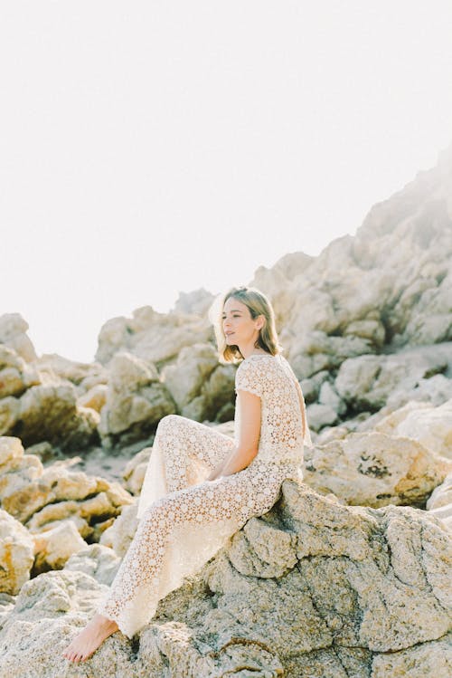 회색 바위에 앉아 흰색 레이스 드레스 여자
