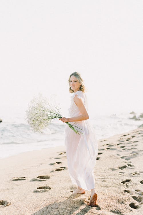 Frau Im Weißen ärmellosen Kleid, Das Weißen Blumenstrauß Am Strand Hält