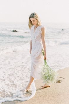 在一个宁静的夏天，金发碧眼的女人拿着鲜花走在海滩上