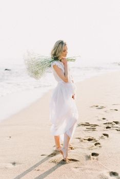 一位白衣女子赤脚站在海浪与鲜花的海滩上，神情宁静