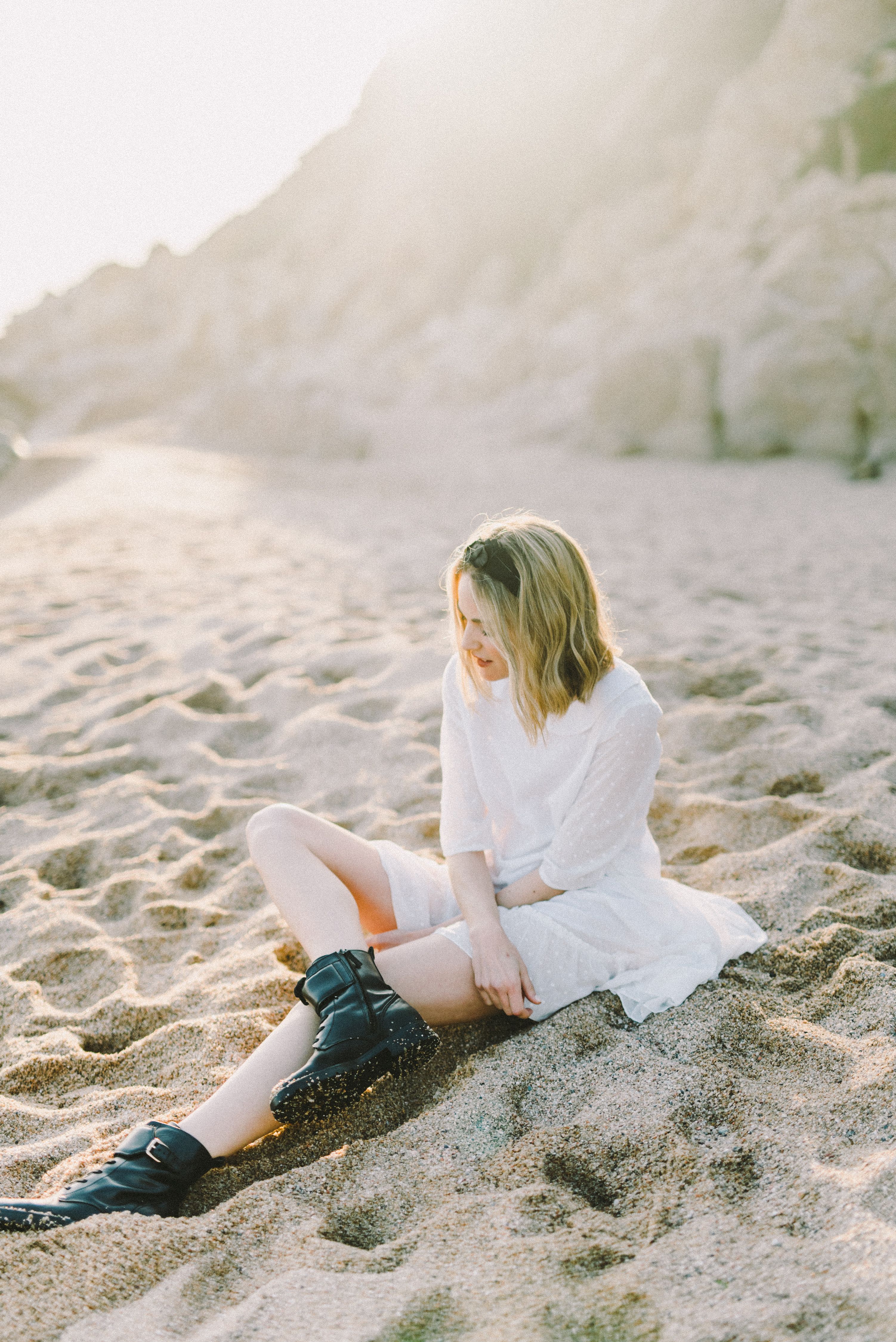 Woman in White Dress and Black Boots Sitting on Sand · Free Stock Photo