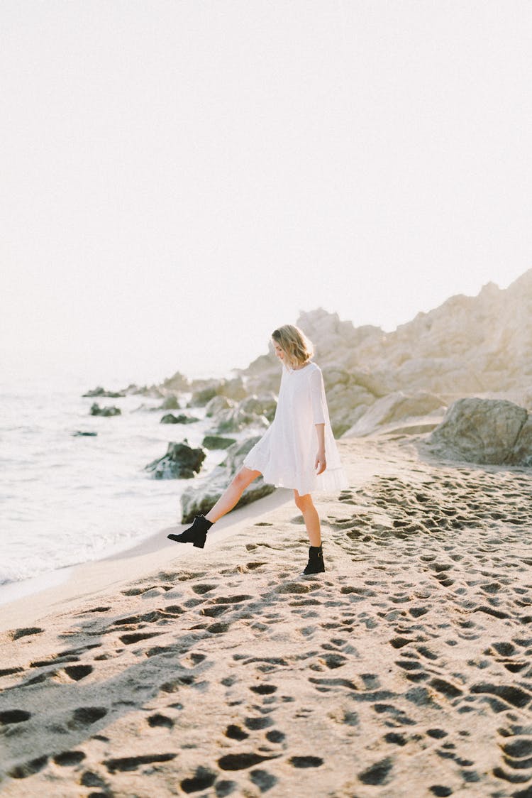 Woman In White Dress And Black Boots Walking On Beach