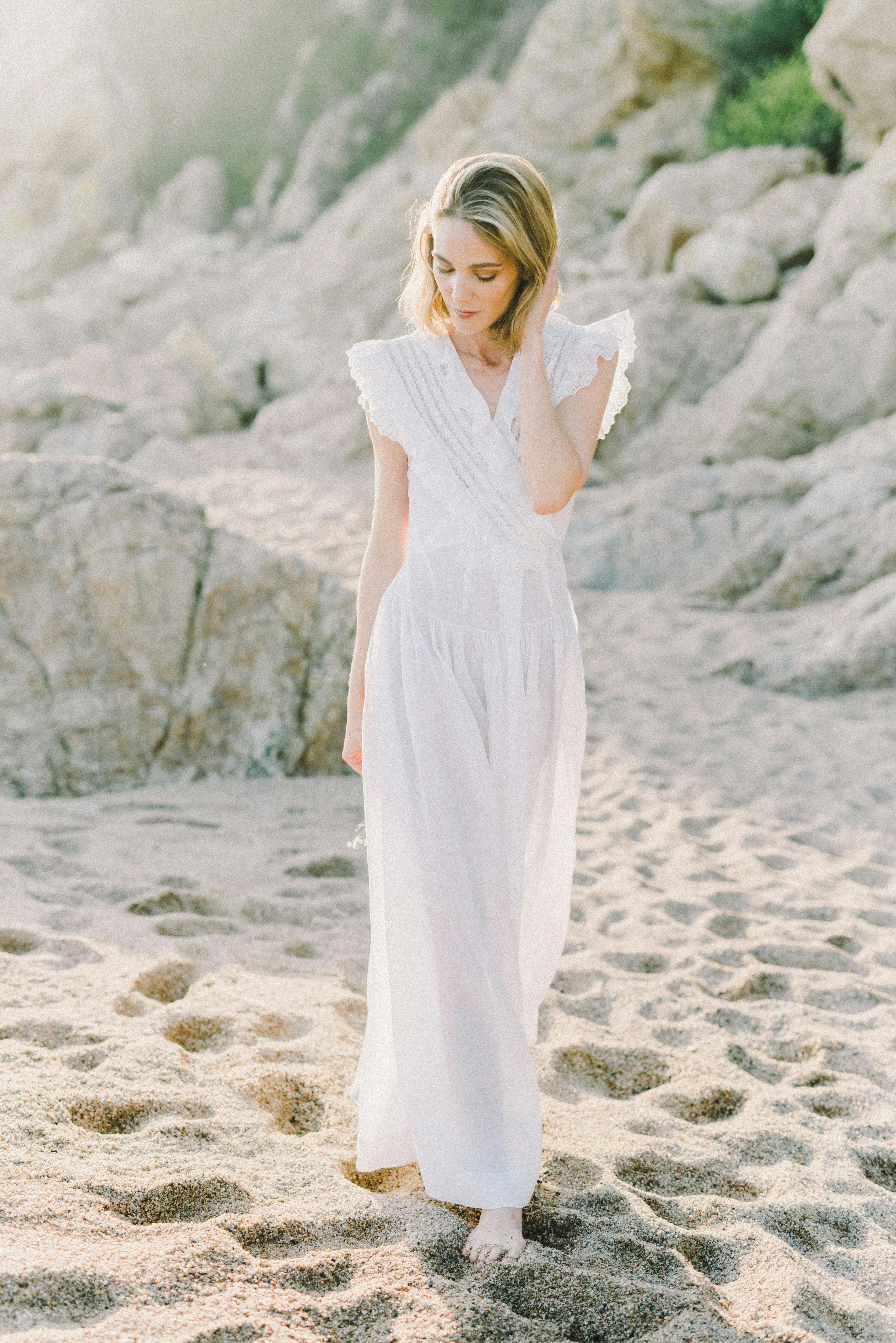 白天，一位身着飘逸白色连衣裙的女子在沙滩上悠闲地散步