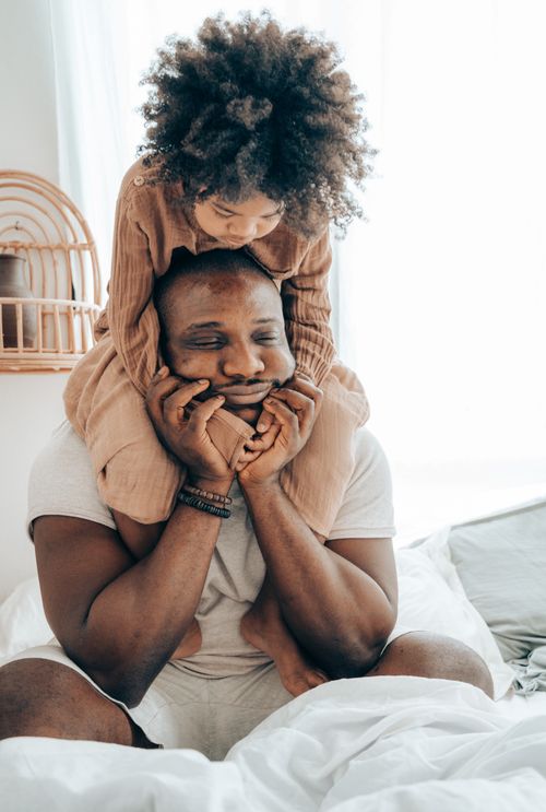 Free Joyful African American child sitting around neck of parent and hugging father during weekend in cozy apartment on daytime Stock Photo