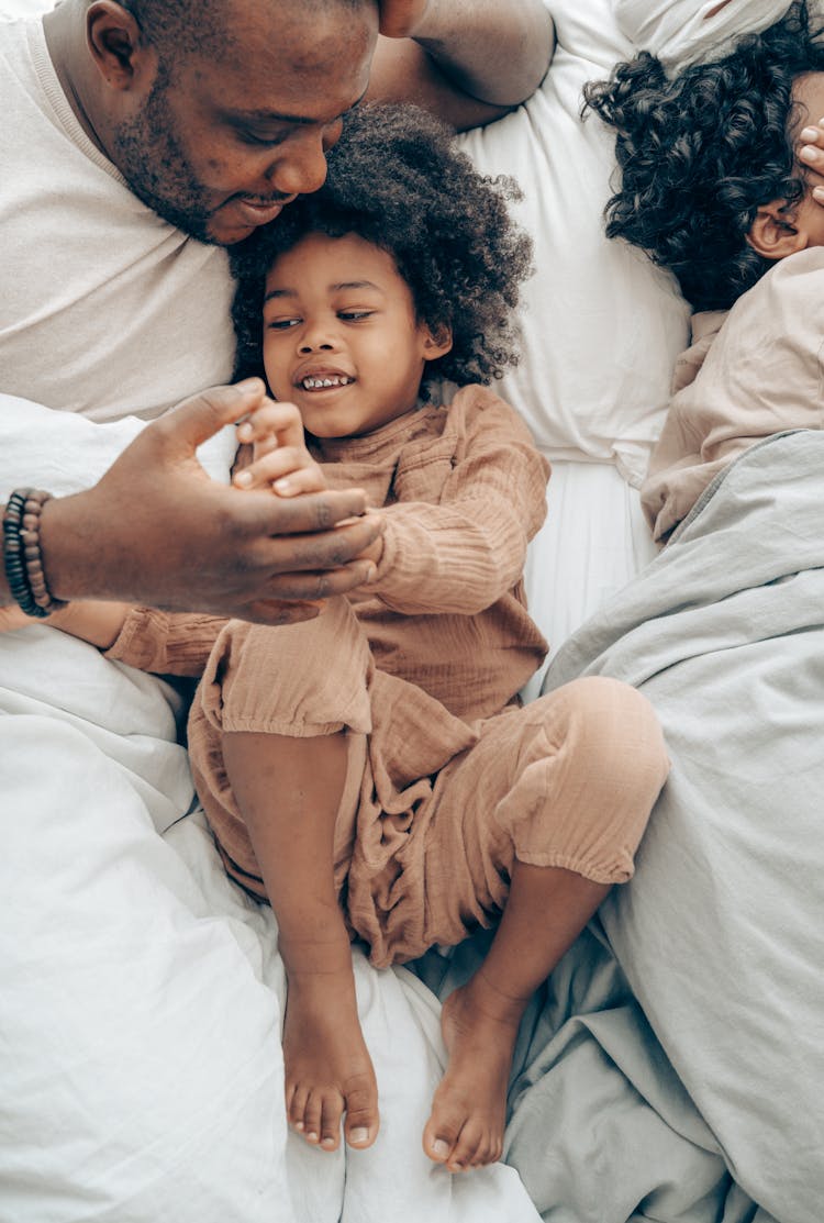 Ethnic Man Playing With Kid In Bedroom