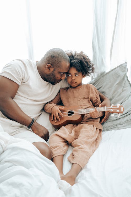 Free Ethnic kid with guitar and father on bed at home Stock Photo