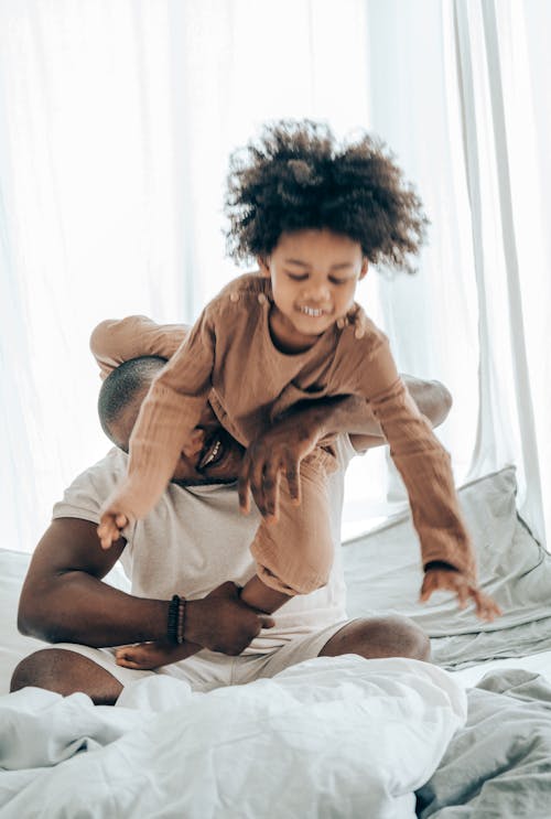 Black dad and kid playing on bed at home