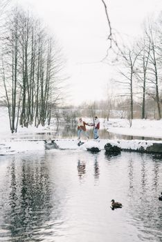 一对夫妇手牵着手，穿过白雪皑皑的河流，河流四周环绕着冬日的森林