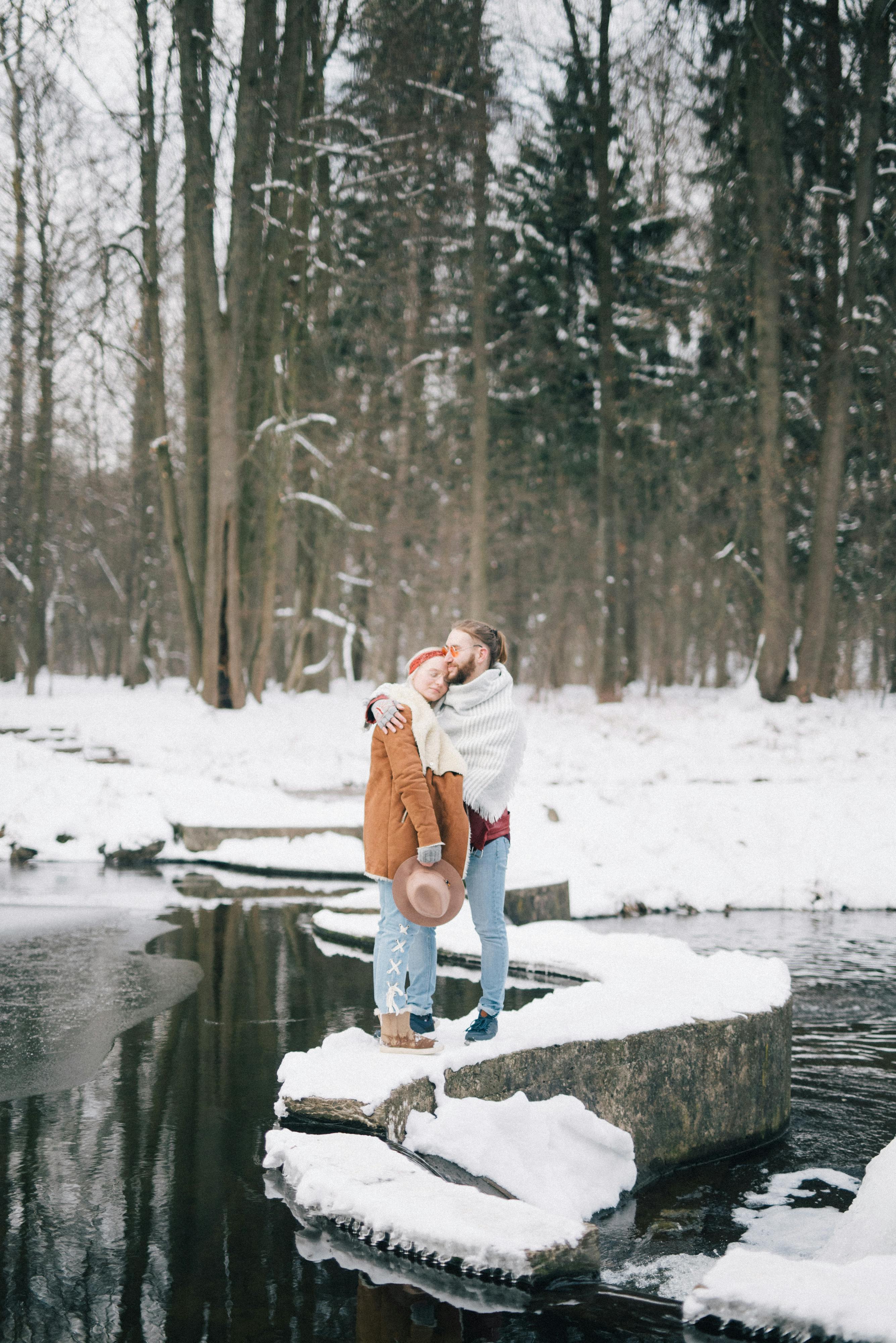 在宁静的冬季公园里，一对夫妇在白雪覆盖的河边拥抱