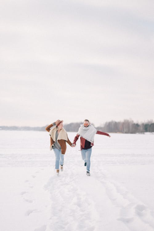 Free Man and Woman Holding Hands while Walking on Snow Covered Ground Stock Photo