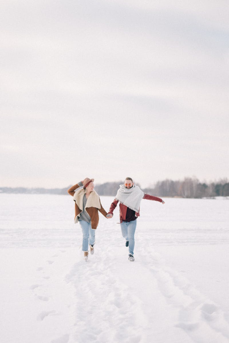 Man and Woman Holding Hands while Walking on Snow Covered Ground