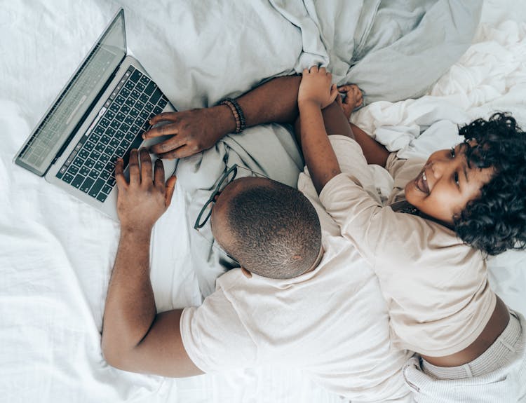 Ethnic Child And Man With Laptop On Bed At Home