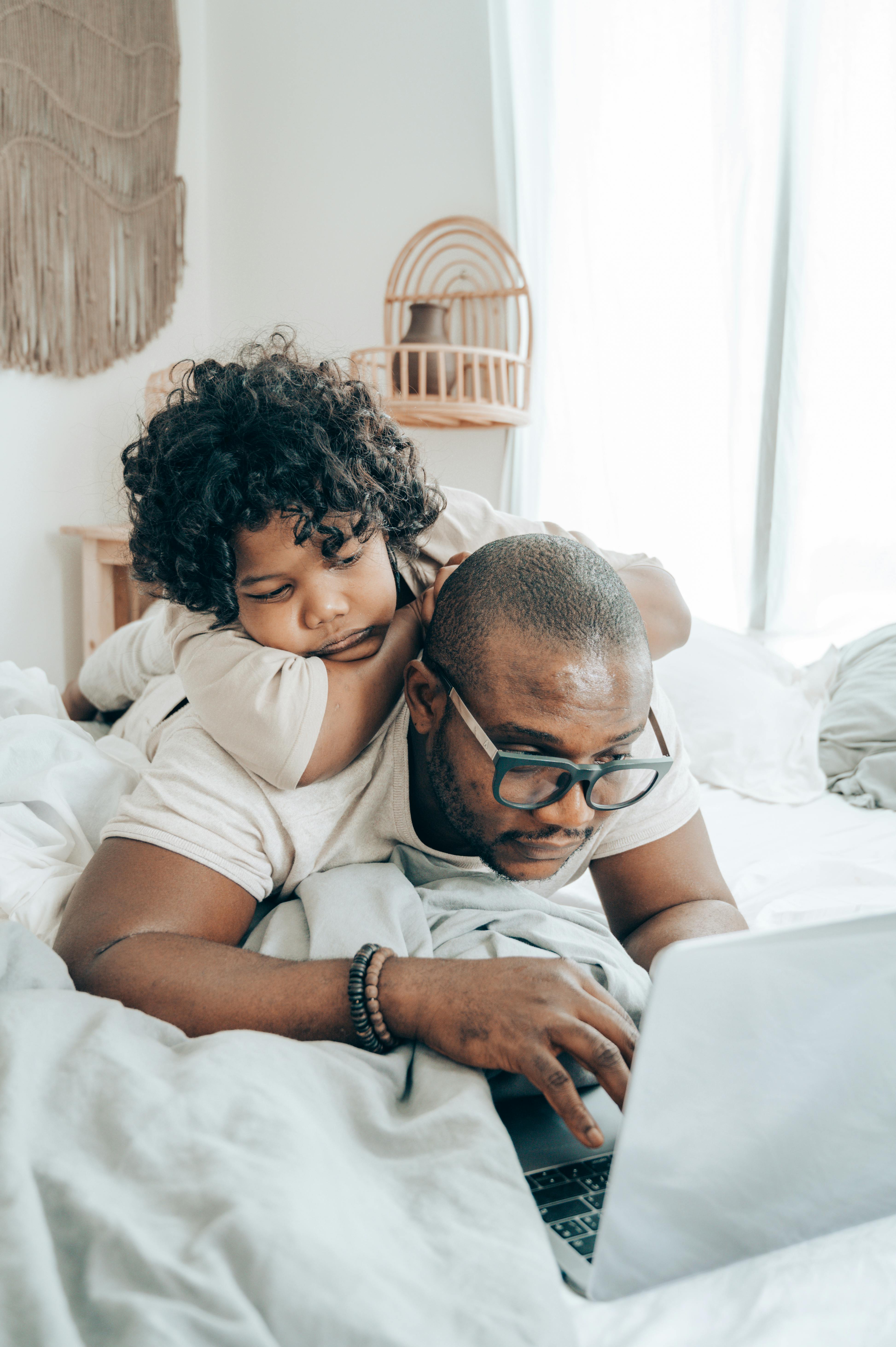 black father and kid browsing laptop together in bedroom