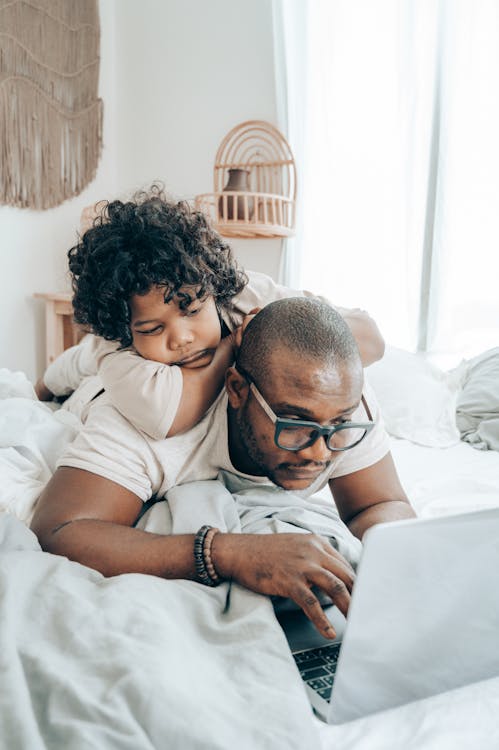 Black father and kid browsing laptop together in bedroom