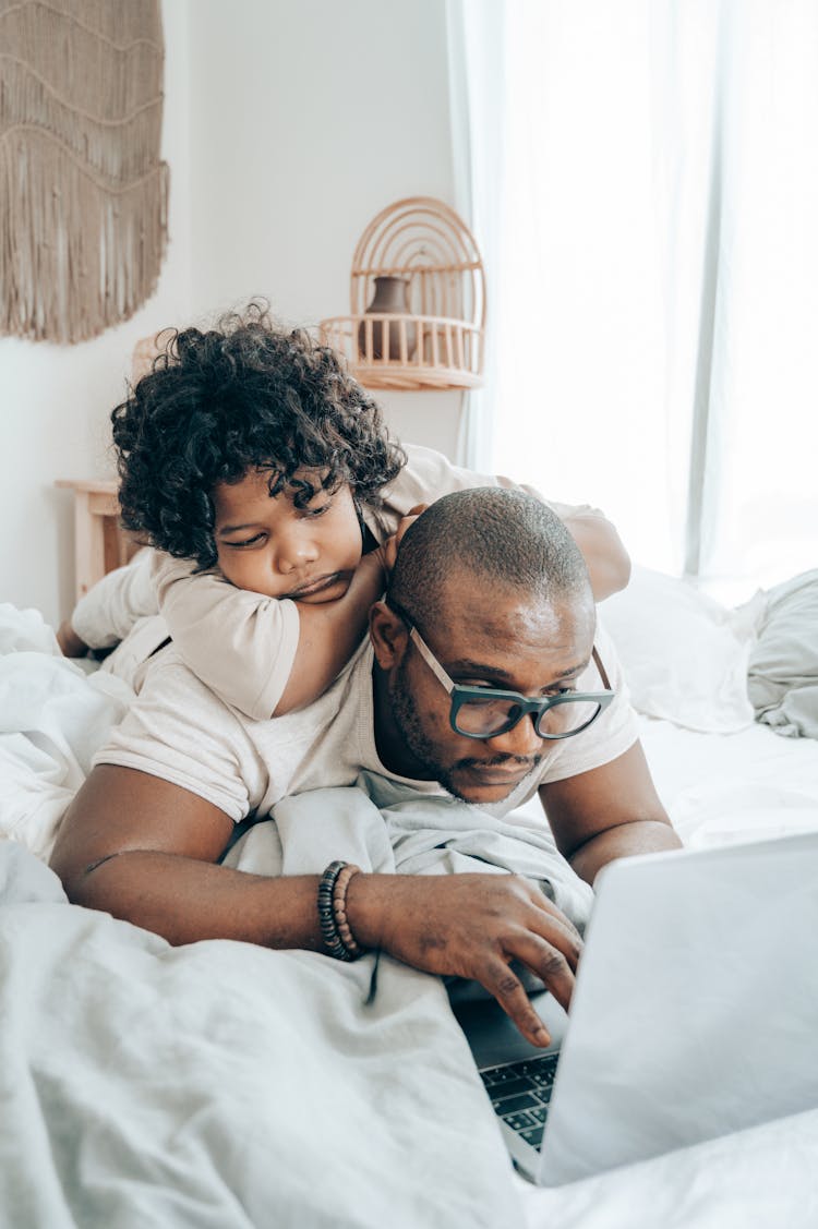 Black Father And Kid Browsing Laptop Together In Bedroom