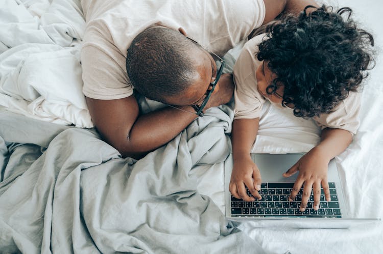 Black Guy And Kid With Laptop In Cozy Bedroom