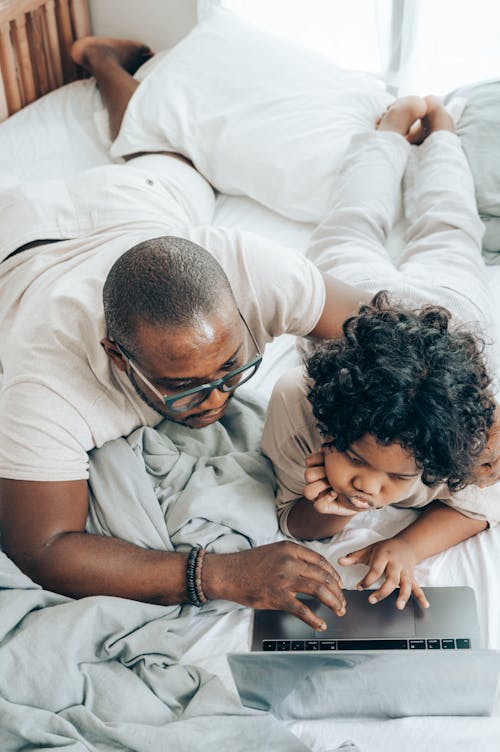 Ethnic man and child using laptop together at home