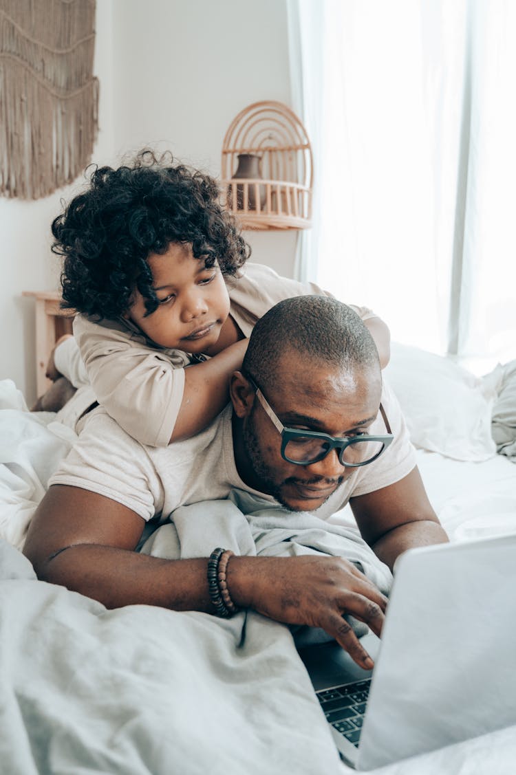 Black Man And Kid Browsing Laptop In Bedroom