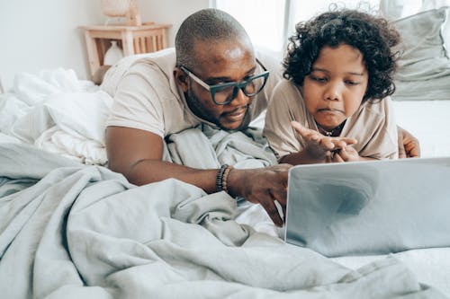 Free Serious man and child with laptop on bed Stock Photo