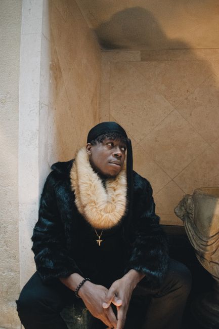 African American man in fur coat sitting indoors in Los Angeles, reflecting urban style.