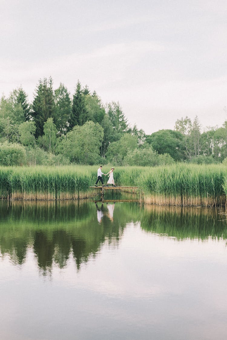 Couple Walking On Wooden Dock Near Lake