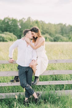 一对夫妇在绿意盎然的田野木栅栏旁，分享了一个亲密的时刻
