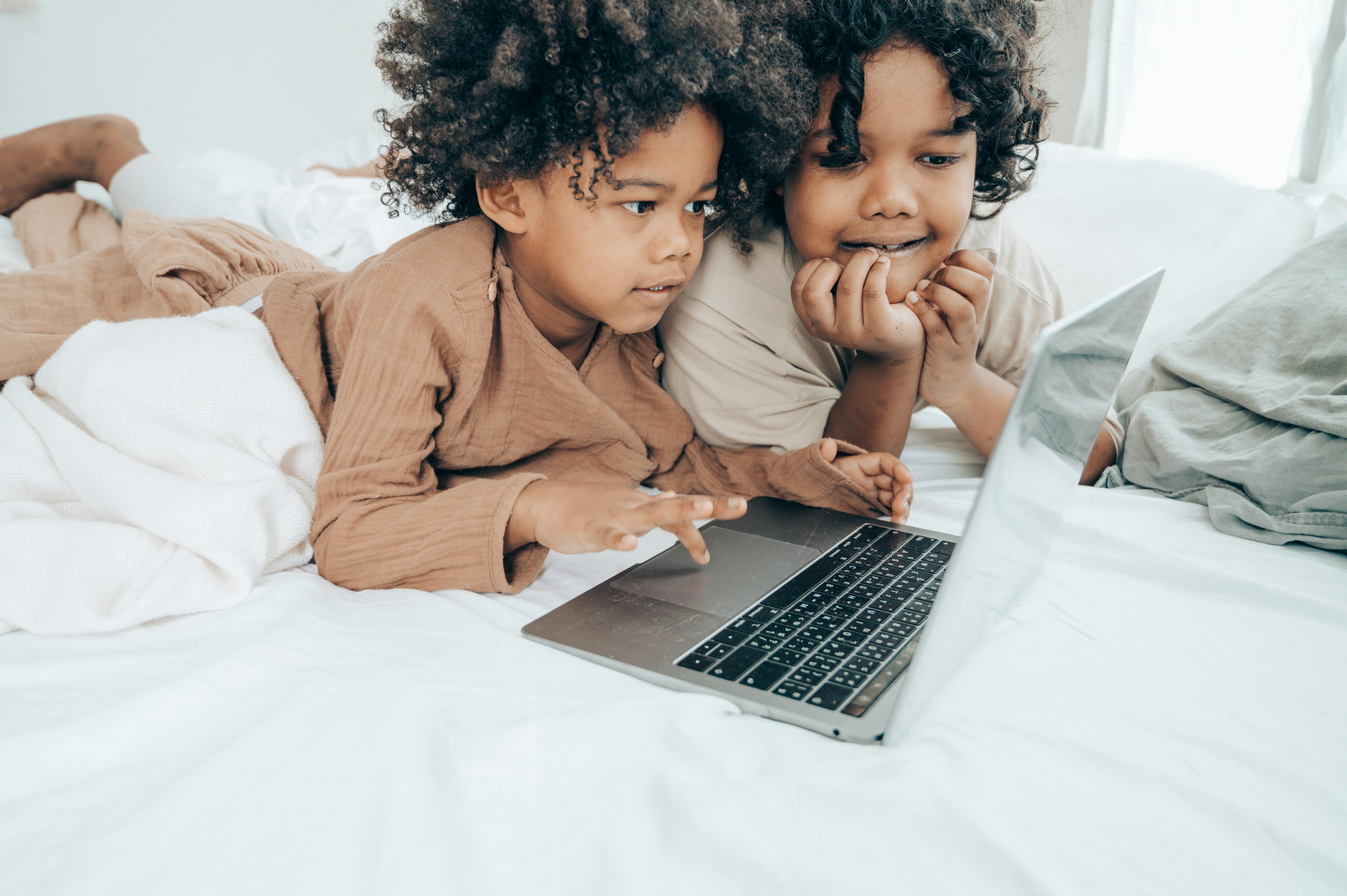 ethnic brothers using laptop on bed