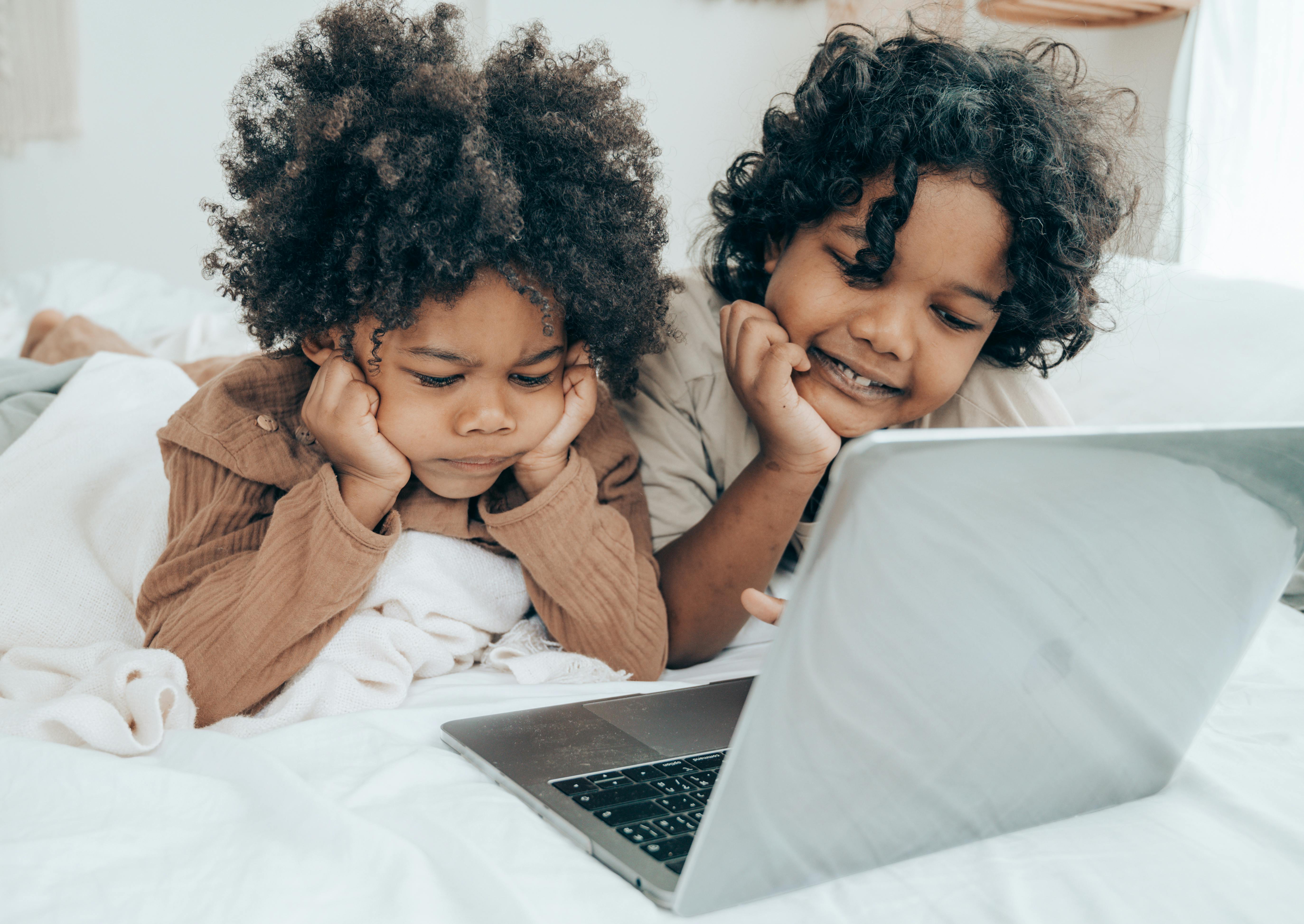 ethnic little brothers using laptop on bed