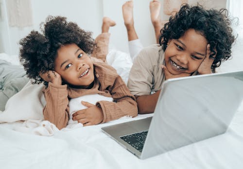 Smiley black boys watching funny video on laptop on bed
