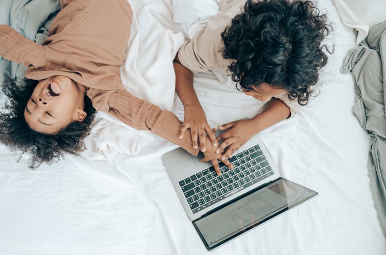 Black Little Child Fooling Around Brother Using Laptop On Bed