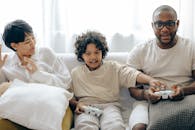 Interested ethnic kid preventing father from winning in video game while resting together with mother in living room