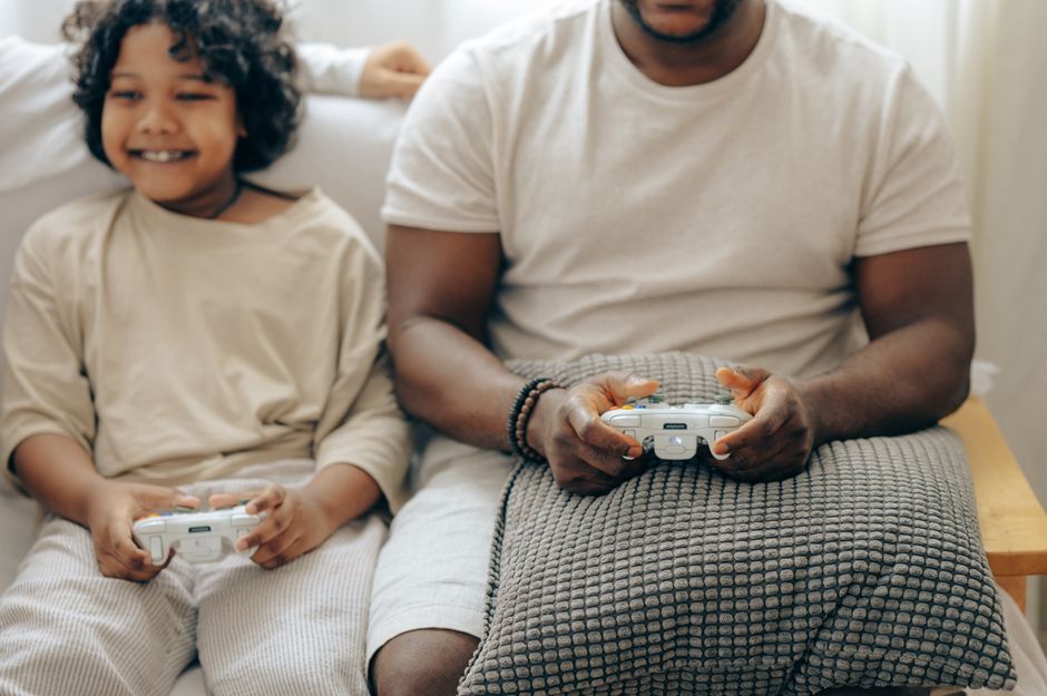Crop black man and son in sleepwear playing video games on console with joysticks while spending time at home together