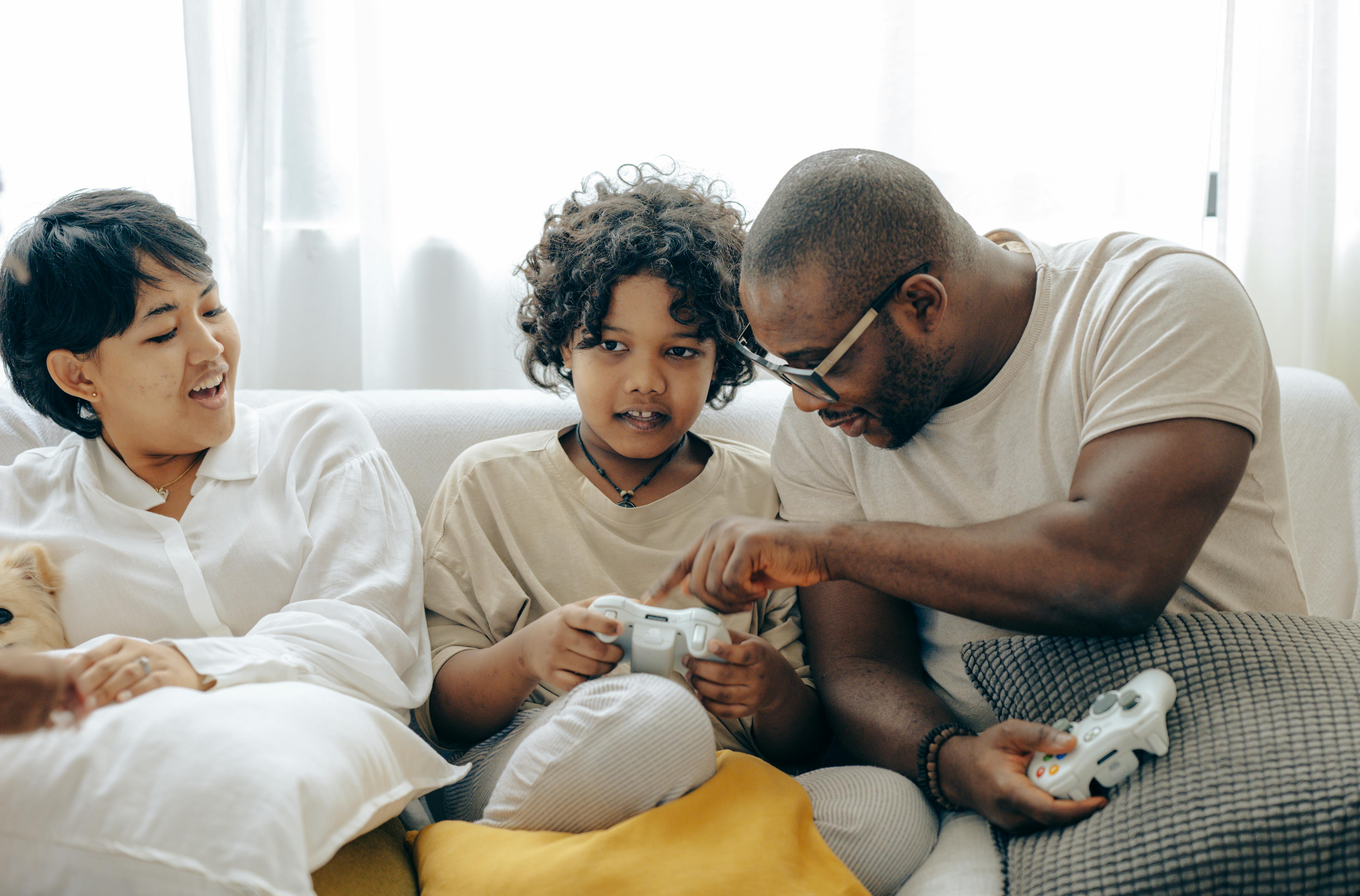 african american father showing on joystick of son teaching rules of playing video game